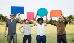 Young people in a grassy field holding word bubbles.