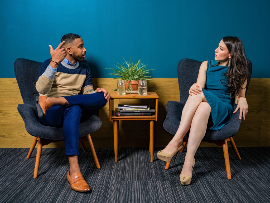 Woman in teal dress sitting and talking with man.