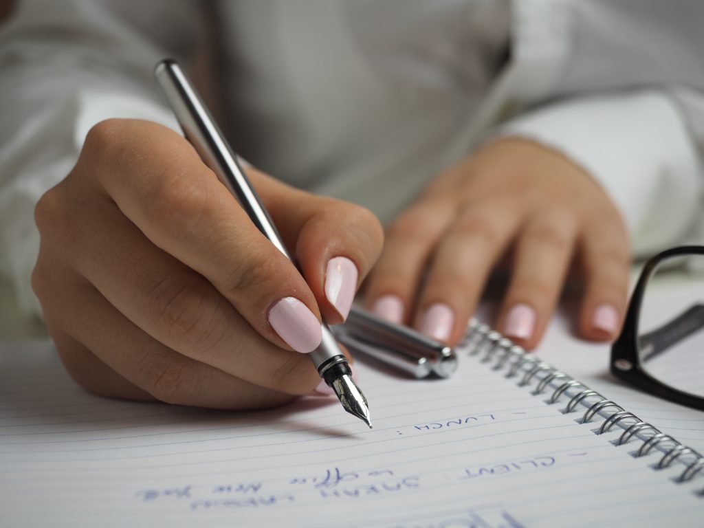 Woman with pink nails writing a to do list.