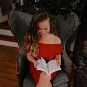 Young woman in a read dress sitting and reading in an armchair