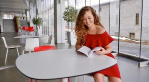 Young woman in red dress sitting at a white table reading a book