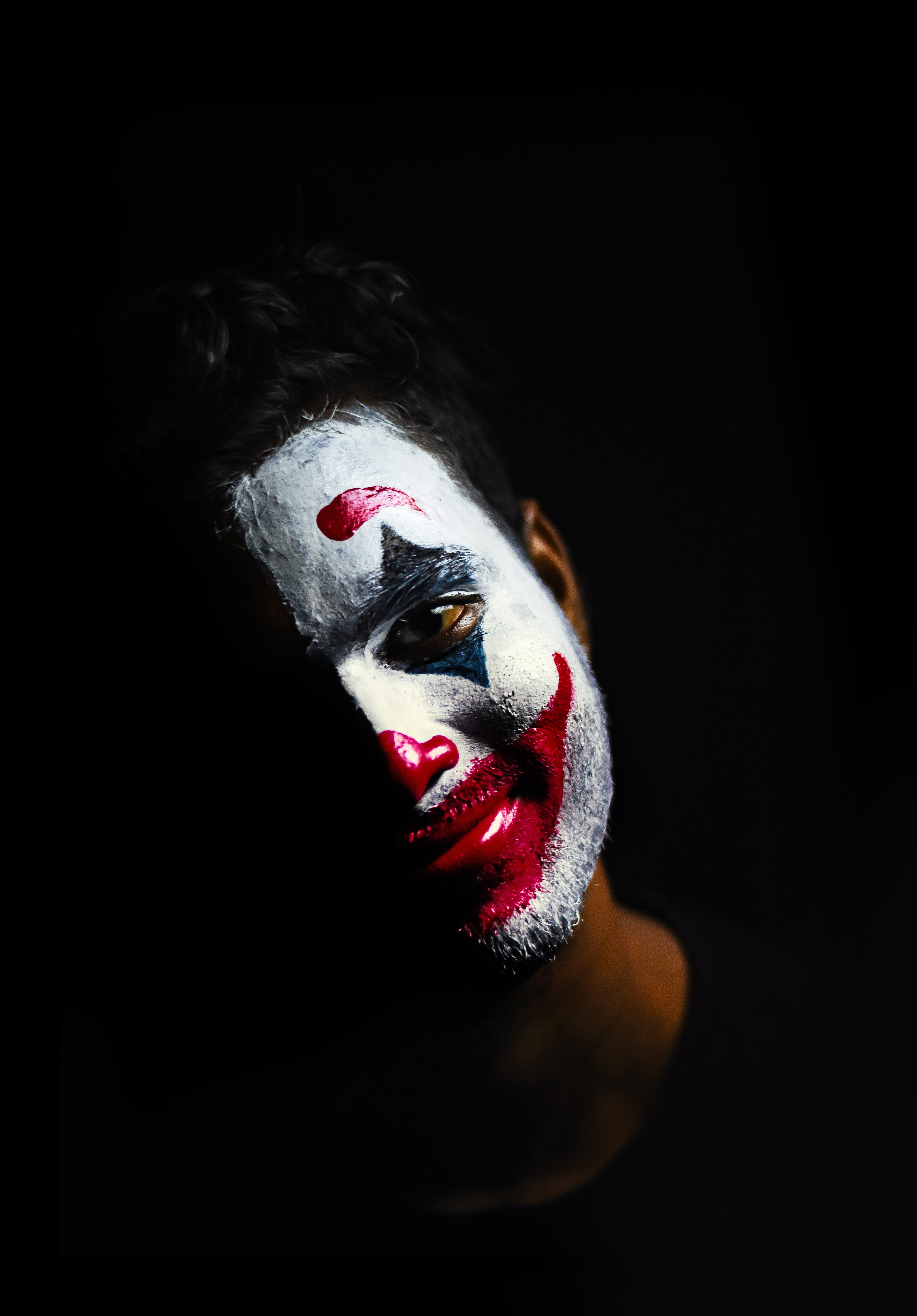 A figure wearing clown makeup is pictured against a black background.